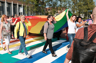 Nel Douw en Sabine Kockx lopen samen met vele belangstellenden over het Regenboogzebrapad